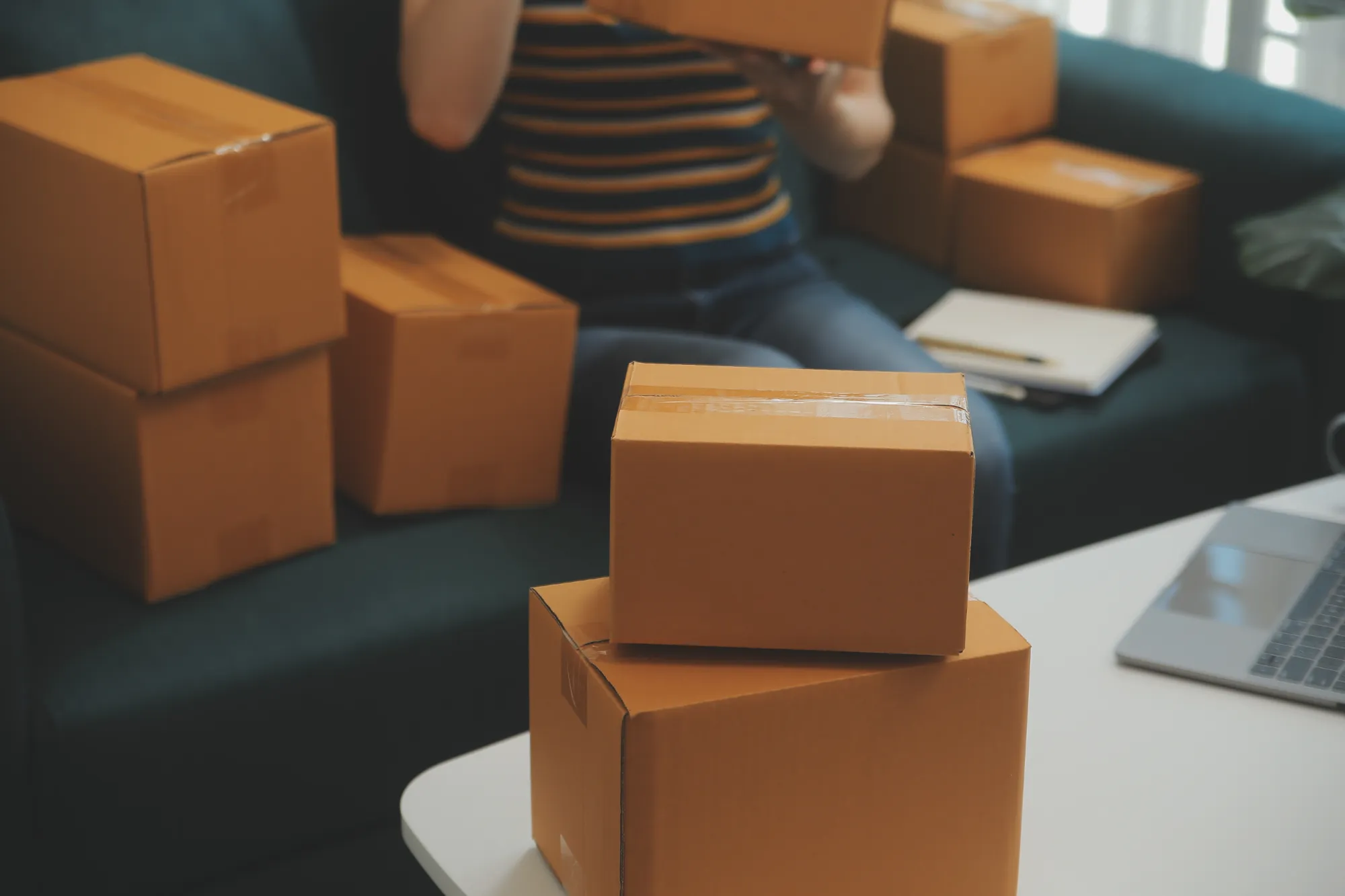 Person sitting on a sofa surrounded by cardboard shipping boxes